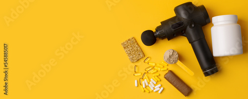 Therapeutic percussive massage gun, fit meal, pills, sport energy bar, protein on yellow background - concept of modern sport activity and diet, health lifestyle routine, wellness, healthcare