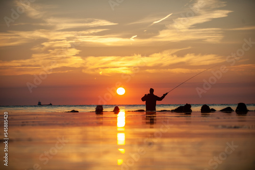 Rear view of man fishing in sea at sunset