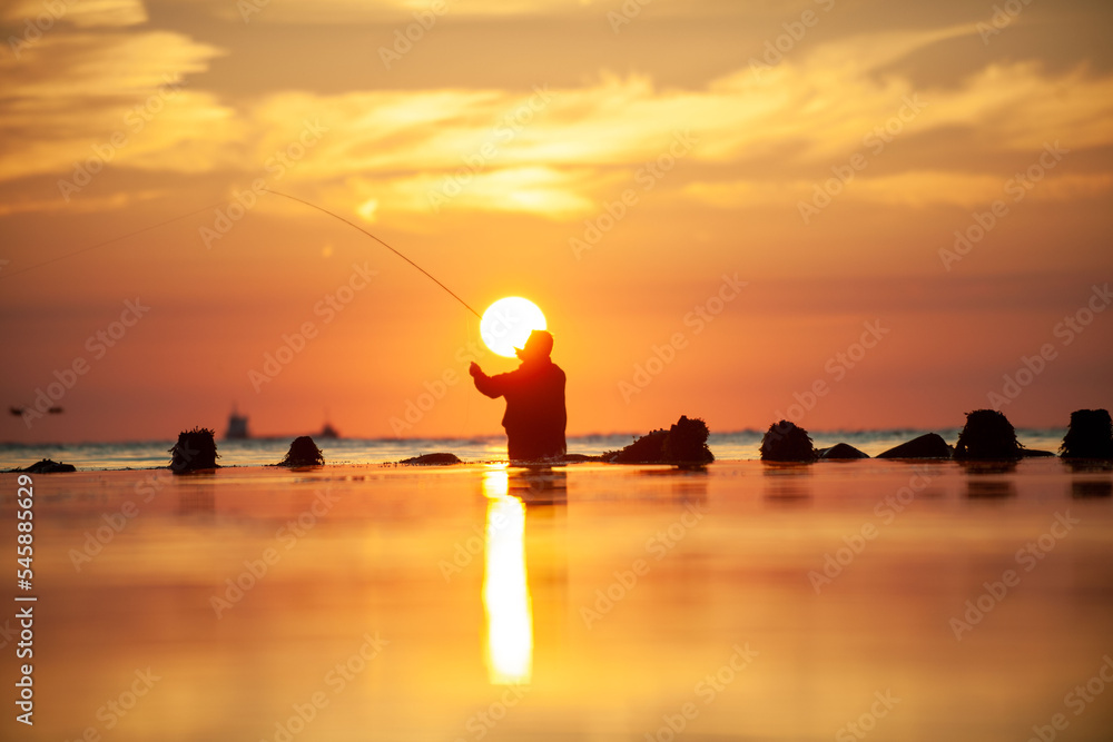 Rear view of man fishing in sea at sunset