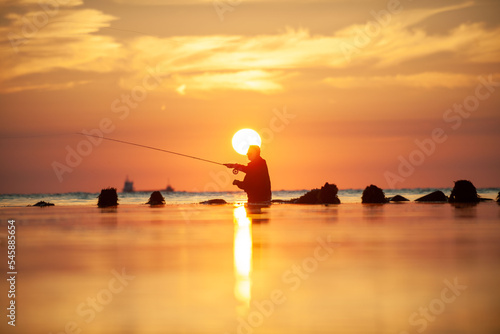 Tableau sur toile Rear view of man fishing in sea at sunset