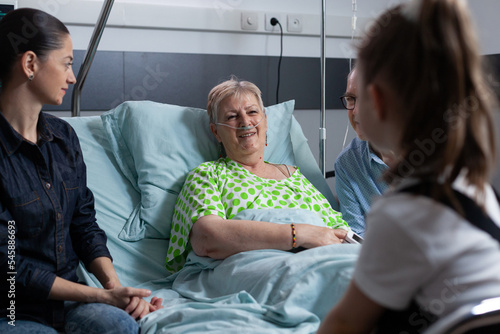 Billede på lærred Smiling elderly woman under medical observation in hospital, chatting happily with girl