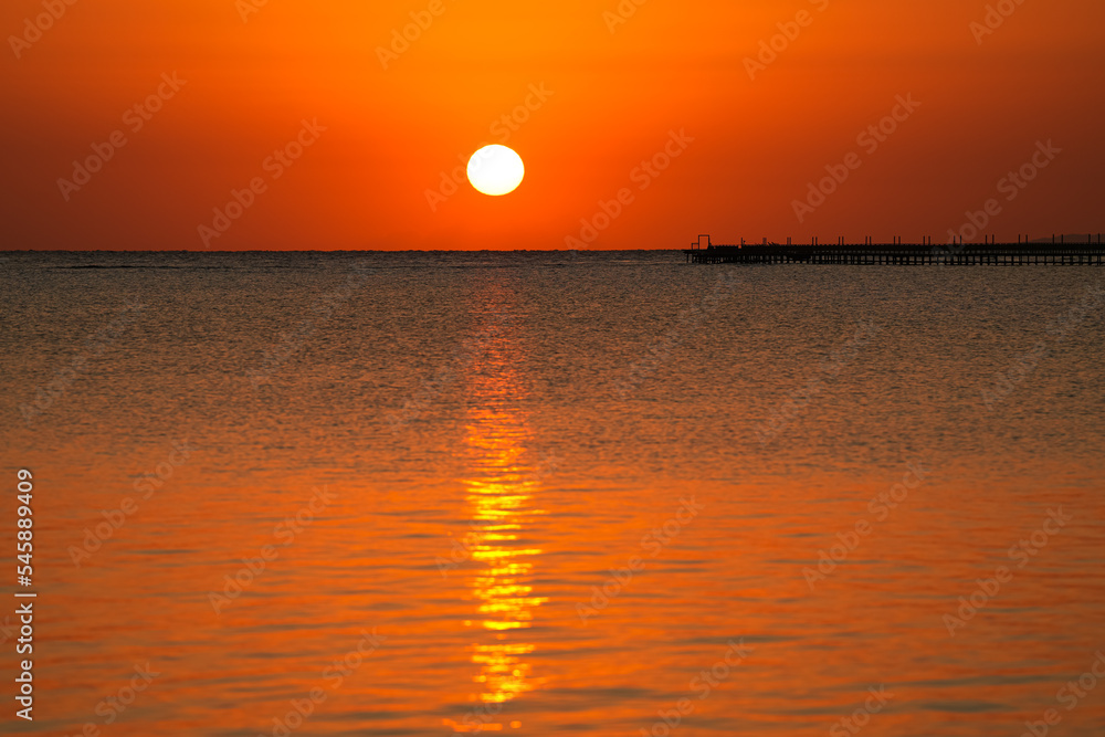 Amazing sunrise landscape from the sea with the silhouette of a wooden pontoon deck in foreground. Beautiful photo at the seaside. Holiday by the sea.