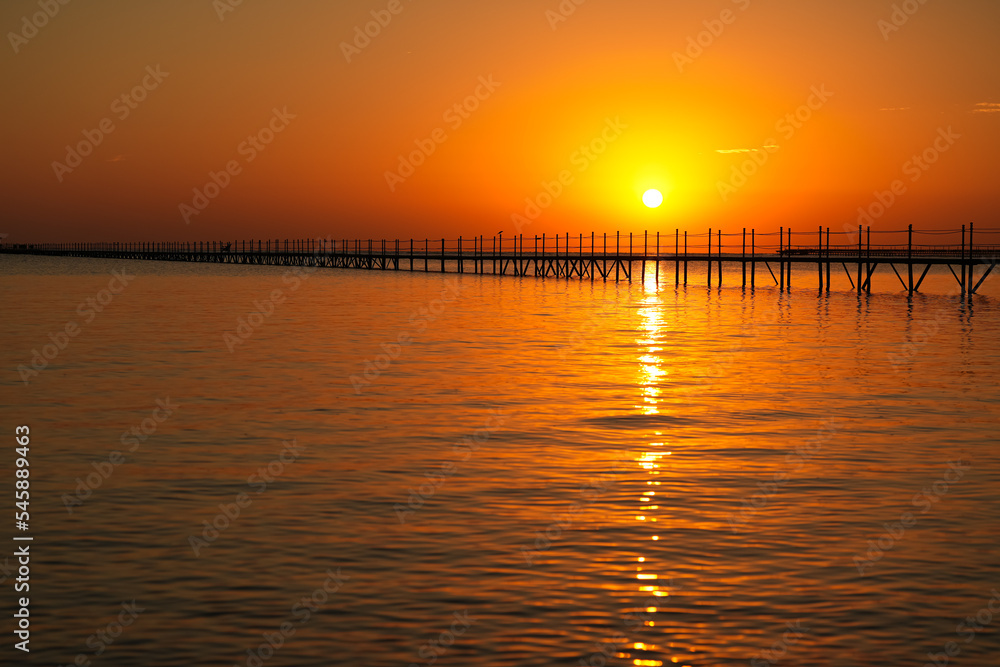 Travel to Sharm el Sheikh. Amazing sunrise from the Red Sea in Egypt. Beautiful photo with the silhouette of a wooden pontoon deck entering the sea.