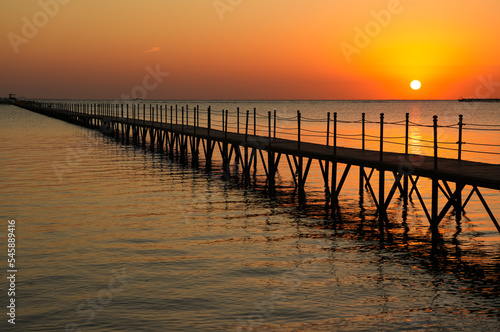 Travel to Sharm el Sheikh. Amazing sunrise from the Red Sea in Egypt. Beautiful photo with the silhouette of a wooden pontoon deck entering the sea.