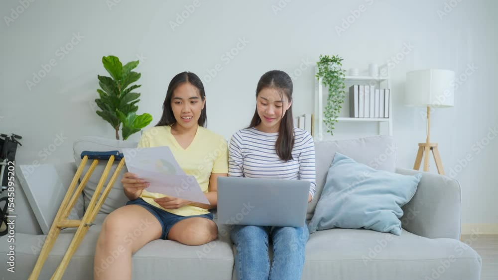 Asian woman amputee using laptop computer with friend in living room. Asian woman amputee using laptop computer with friend in living room.