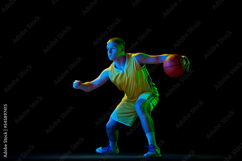 Professional basketball player in action with ball isolated on black background in neon light filter. Dribbling. Sport, energy, skills, team competition