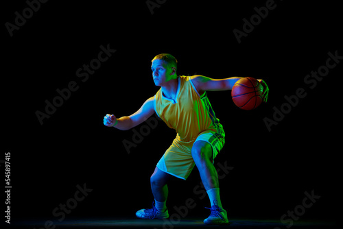 Professional basketball player in action with ball isolated on black background in neon light filter. Dribbling. Sport, energy, skills, team competition