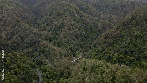 Aerial establishing shot of a tiny, old river bridge within a pristine, mountainous rainforest photo