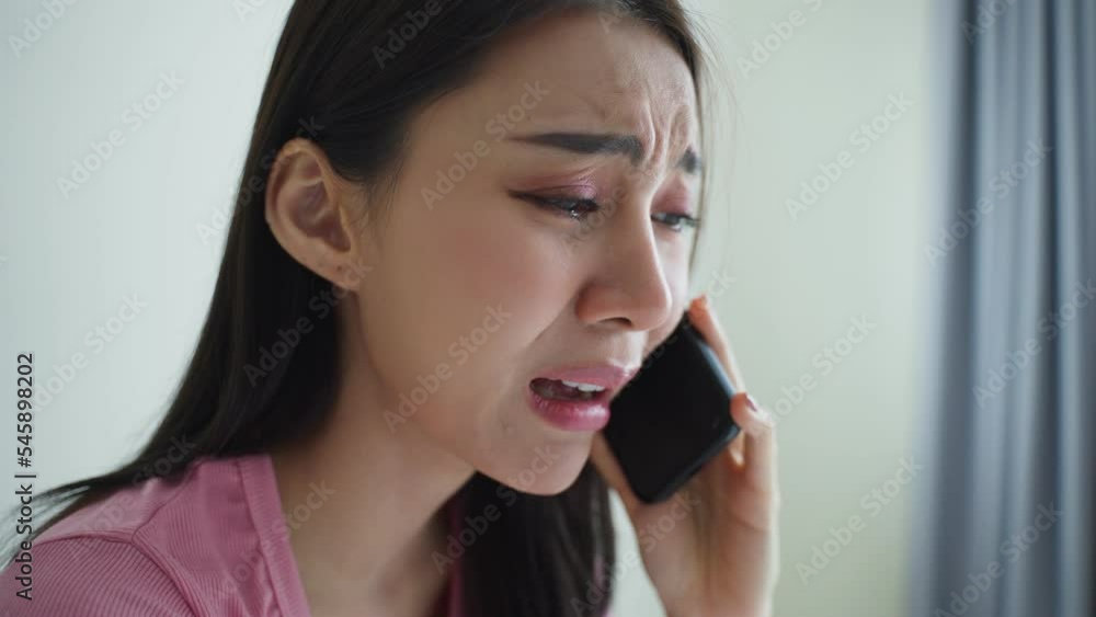 Asian upset depressed woman sitting on bed and talking on mobile phone. Asian upset depressed woman sitting on bed and talking on mobile phone.