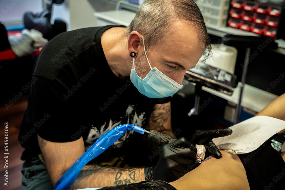 Tattooist concentrating while working on the skin of an unrecognizable woman - concept of work and concentration