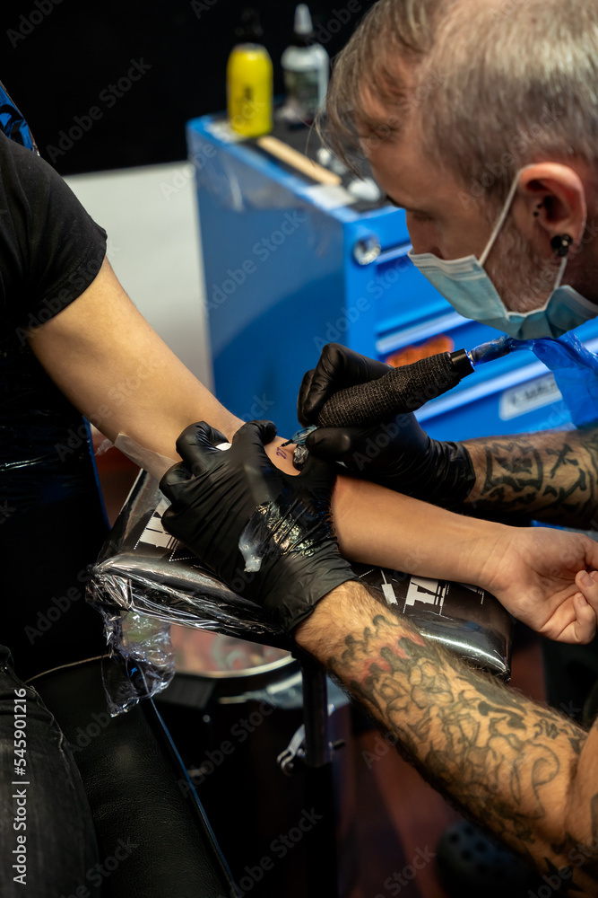 Tattoo artist tattooing an unrecognizable woman on her arm - concept of work and art