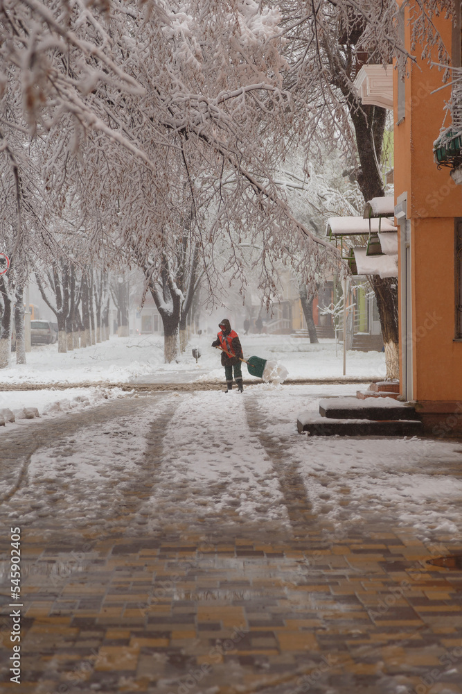 Janitor or sweeper in orange jacket cleaning city streets from snow with showel. snow removal in park