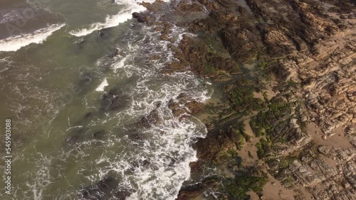 high drone flight over a surfer entering the rough seas of the Atlantic Ocean near the rocky shores of Punta del Este in Uruguay