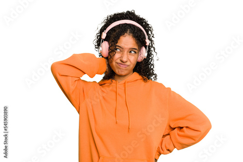 Young Brazilian woman listening to music with headphones isolated touching back of head, thinking and making a choice.