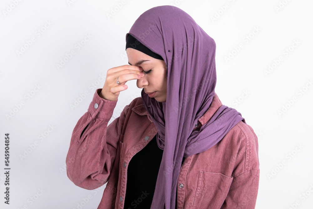 Sad young beautiful muslim woman wearing hijab against white background suffering from headache holding hand on her face Sad young beautiful muslim woman wearing hijab against white background suffering from headache holding hand on her face
