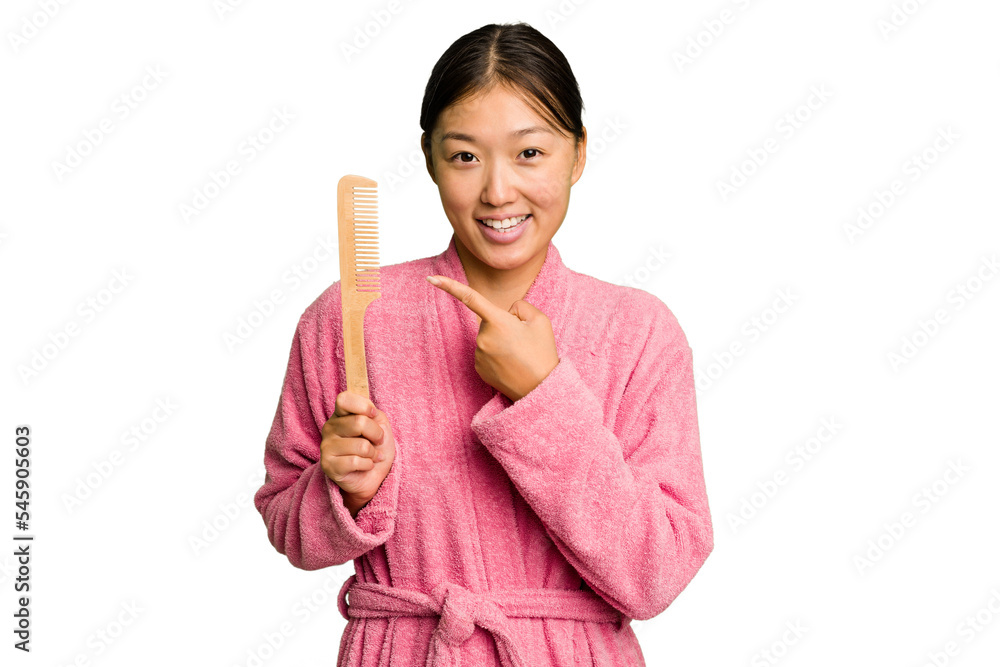 Young asian woman holding an hair comb isolated smiling and pointing aside, showing something at blank space. Young asian woman holding an hair comb isolated smiling and pointing aside, showing something at blank space.