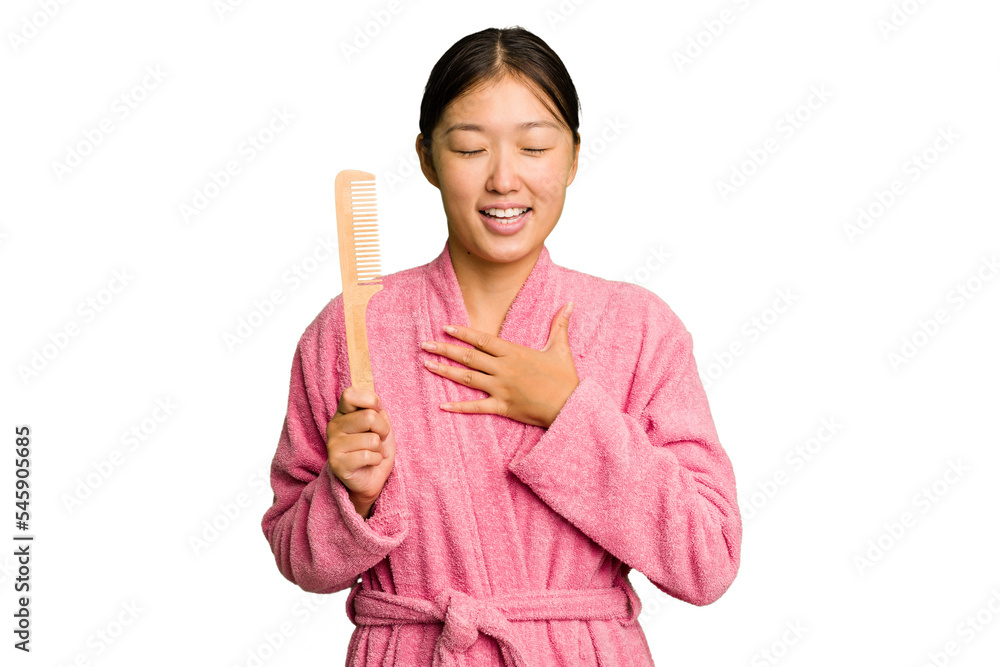 Young asian woman holding an hair comb isolated laughs out loudly keeping hand on chest. Young asian woman holding an hair comb isolated laughs out loudly keeping hand on chest.