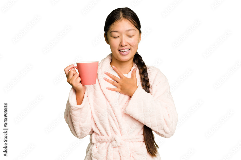 Young asian woman wearing a pajama holding a cup isolated laughs out loudly keeping hand on chest. Young asian woman wearing a pajama holding a cup isolated laughs out loudly keeping hand on chest.