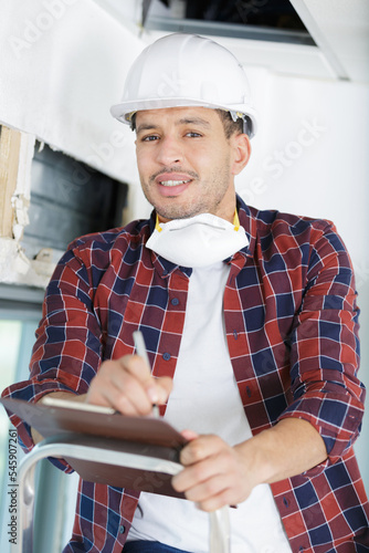 home inspector on a ladder while writing on a clipboard