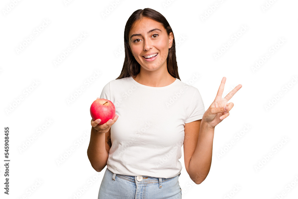 Young caucasian woman holding a red apple isolated joyful and carefree showing a peace symbol with fingers. Young caucasian woman holding a red apple isolated joyful and carefree showing a peace symbol with fingers.