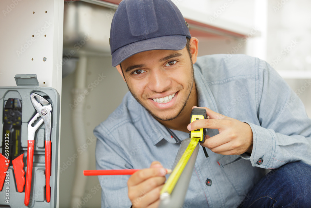 portrait of young plumber measuring length of pipe portrait of young plumber measuring length of pipe