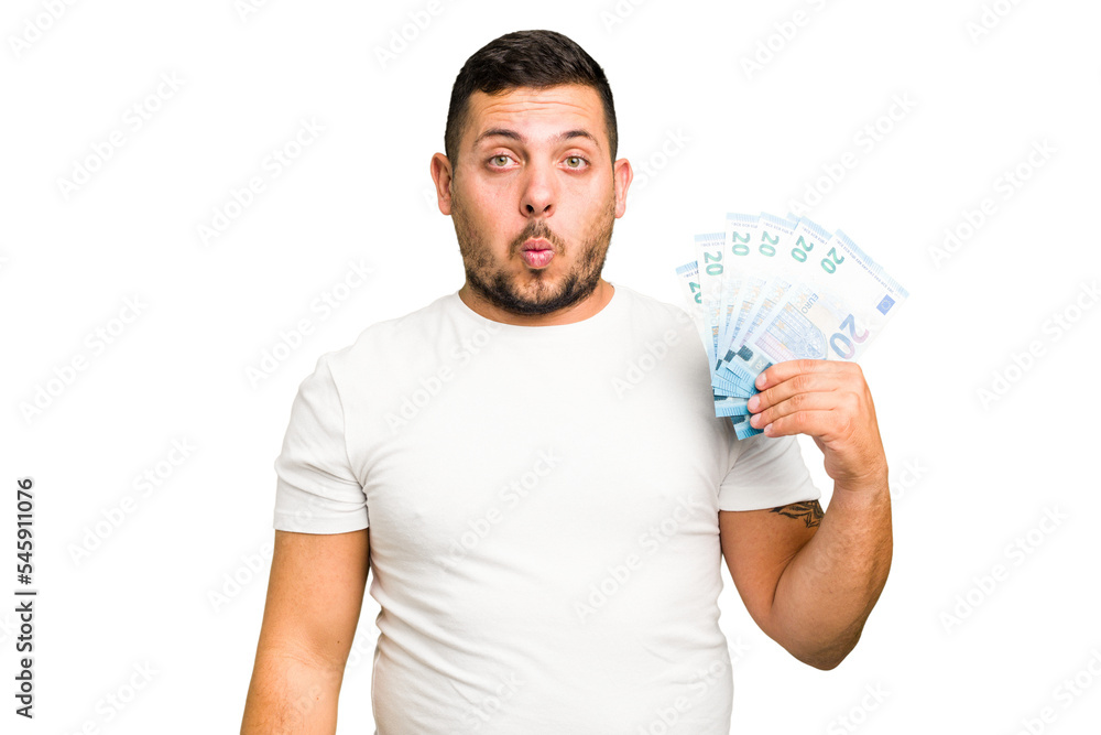 Young caucasian man holding a banknotes isolated shrugs shoulders and open eyes confused. Young caucasian man holding a banknotes isolated shrugs shoulders and open eyes confused.