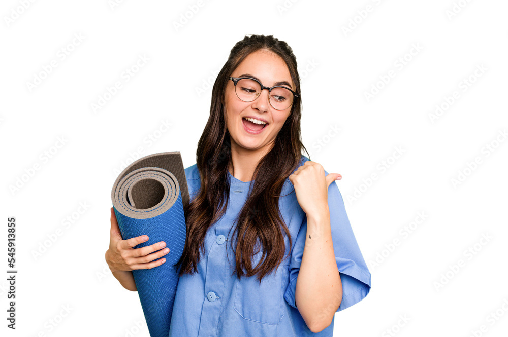 Young caucasian physiotherapist woman holding a mat isolated isolated on green chroma background points with thumb finger away, laughing and carefree.