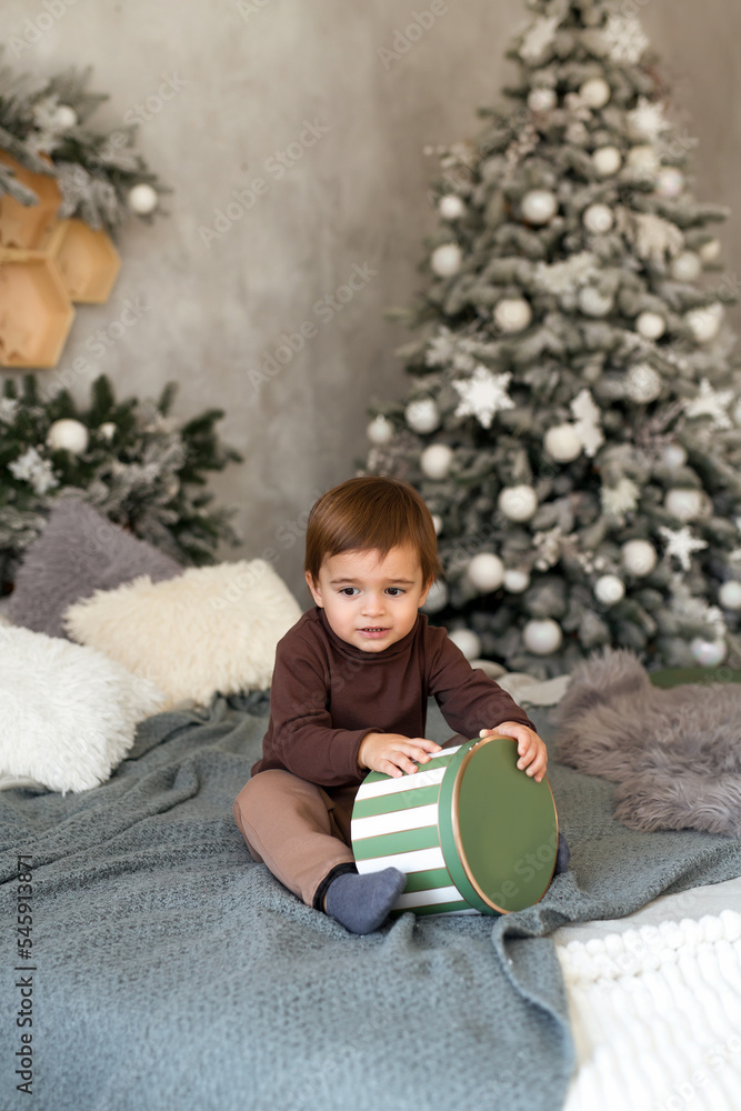 Naklejka premium Cute toddler boy with a Christmas present at home close-up. New Year's comfort at home, bedroom decor.