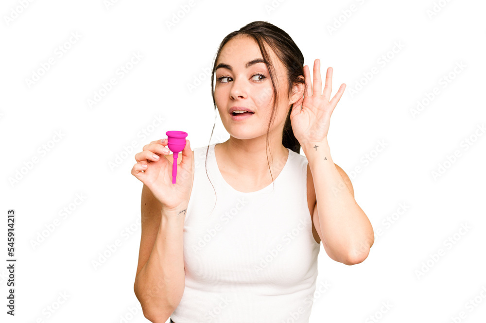 Young caucasian woman holding menstrual cup isolated on green chroma background trying to listening a gossip. Young caucasian woman holding menstrual cup isolated on green chroma background trying to listening a gossip.