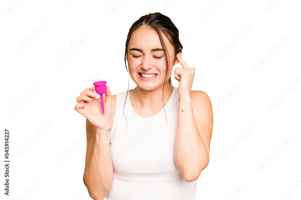 Young caucasian woman holding menstrual cup isolated on green chroma background covering ears with hands. Young caucasian woman holding menstrual cup isolated on green chroma background covering ears with hands.