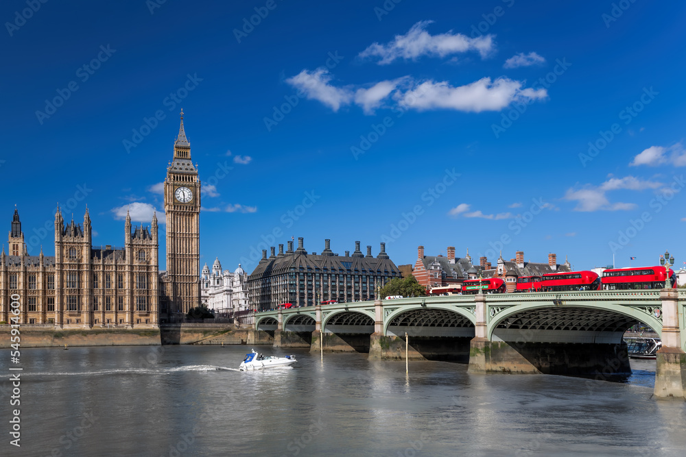 Big Ben with red buses on bridge over Thames river with boat in London, England, UK