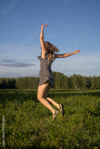 a woman jumps in flight hands in different directions in a summer field in a black sundress