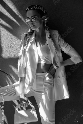 Fashionable woman with braids and white suit on background with exotic flowers and shadows.