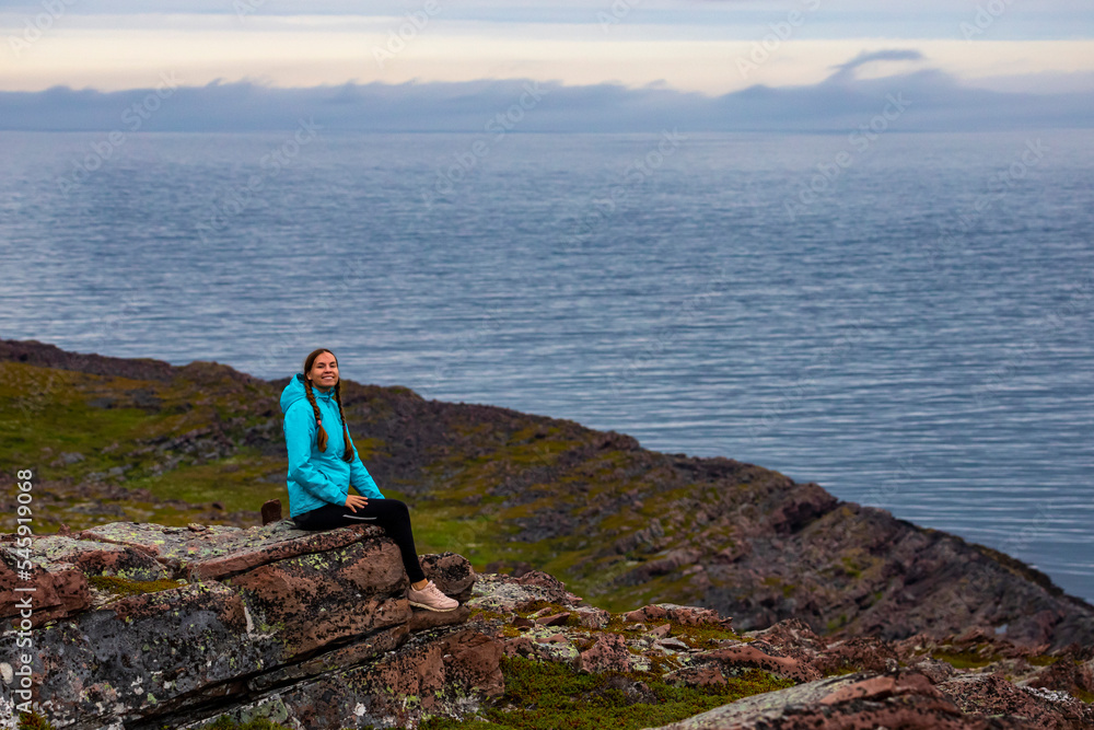 hiker girl sits on rocks by the ocean in northern norway; harsh arctic landscape, relaxing by the sea in the far north