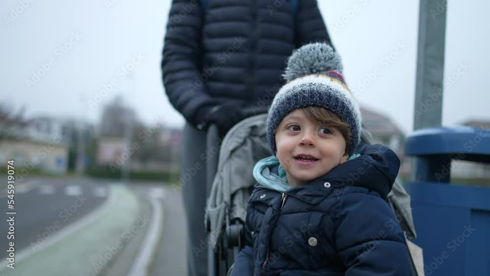 Mother pushing happy little boy on stroller wearing winter clothes. Small child seated on stroll seat with beanie and coat. Closeup face in motion Mother pushing happy little boy on stroller wearing winter clothes. Small child seated on stroll seat with beanie and coat. Closeup face in motion