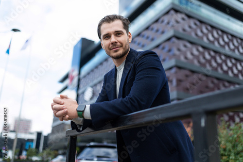 a successful young male businessman in business clothes stands against the backdrop of an office building outside