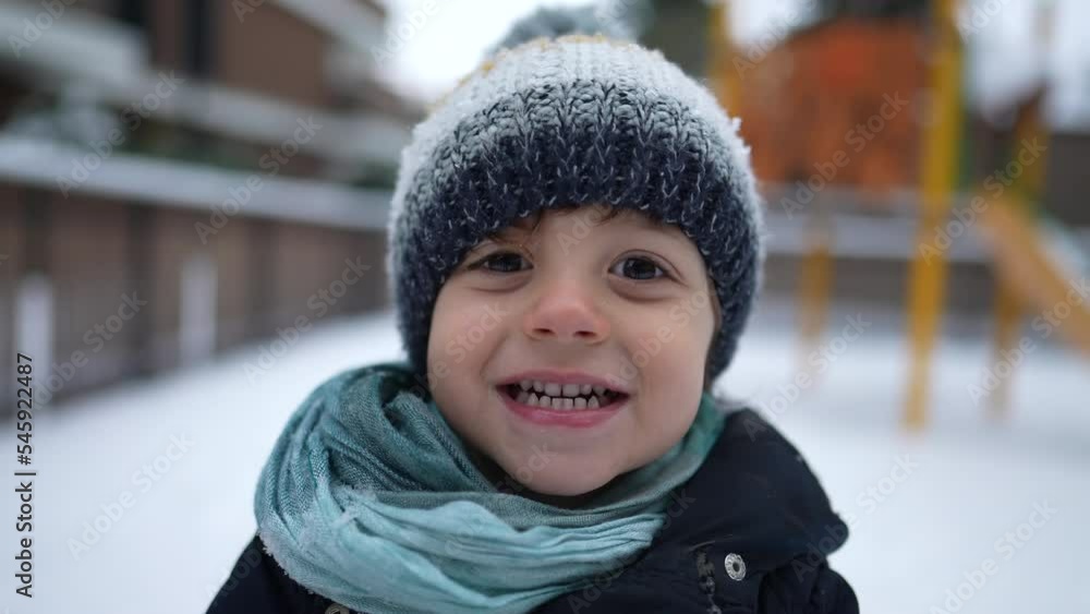 One happy child portrait face in winter season covered in snow. Small boy wearing beanie scarf and coat smiling at camera standing outdoors One happy child portrait face in winter season covered in snow. Small boy wearing beanie scarf and coat smiling at camera standing outdoors