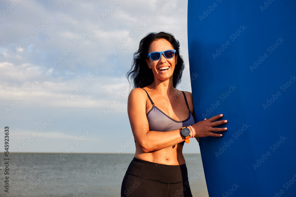 Young smiling woman with surf stands on the beach