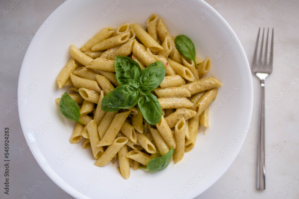 Penne pasta with spinach pesto sauce and basil leaves. High angle view. Selective Focus Basil.
