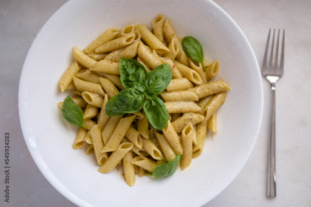 Penne pasta with spinach pesto sauce and basil leaves. High angle view. Selective Focus Basil. Penne pasta with spinach pesto sauce and basil leaves. High angle view. Selective Focus Basil.