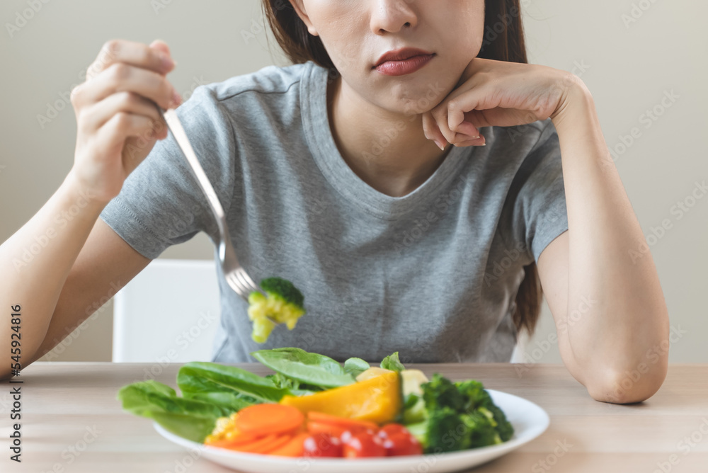 unhappy asian women is on dieting time looking at broccoli on the fork. girl do not want to eat vegetables and dislike taste