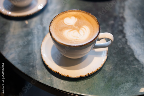 A white ceramic cup with full of latte art coffee on grey table background. Beautiful foam  greenery ceramic cups  stylish toning  place for text.