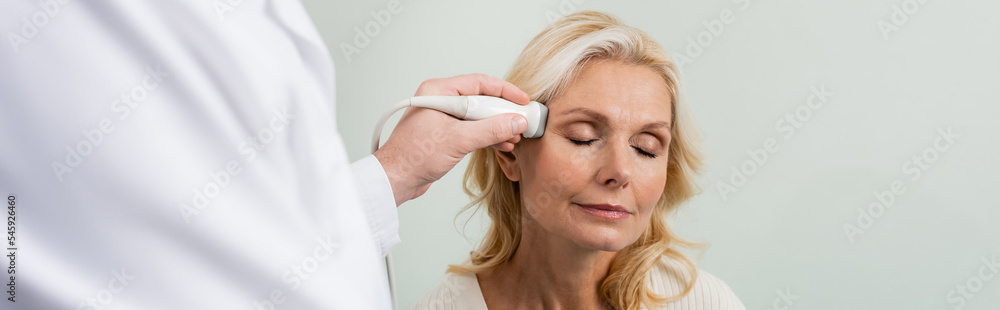 blonde woman with closed eyes near blurred doctor doing ultrasound of her head, banner. blonde woman with closed eyes near blurred doctor doing ultrasound of her head, banner.