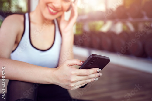 Young woman sitting on yoga mat after exercising, relaxing with smartphone and listening to music. © Thanumporn