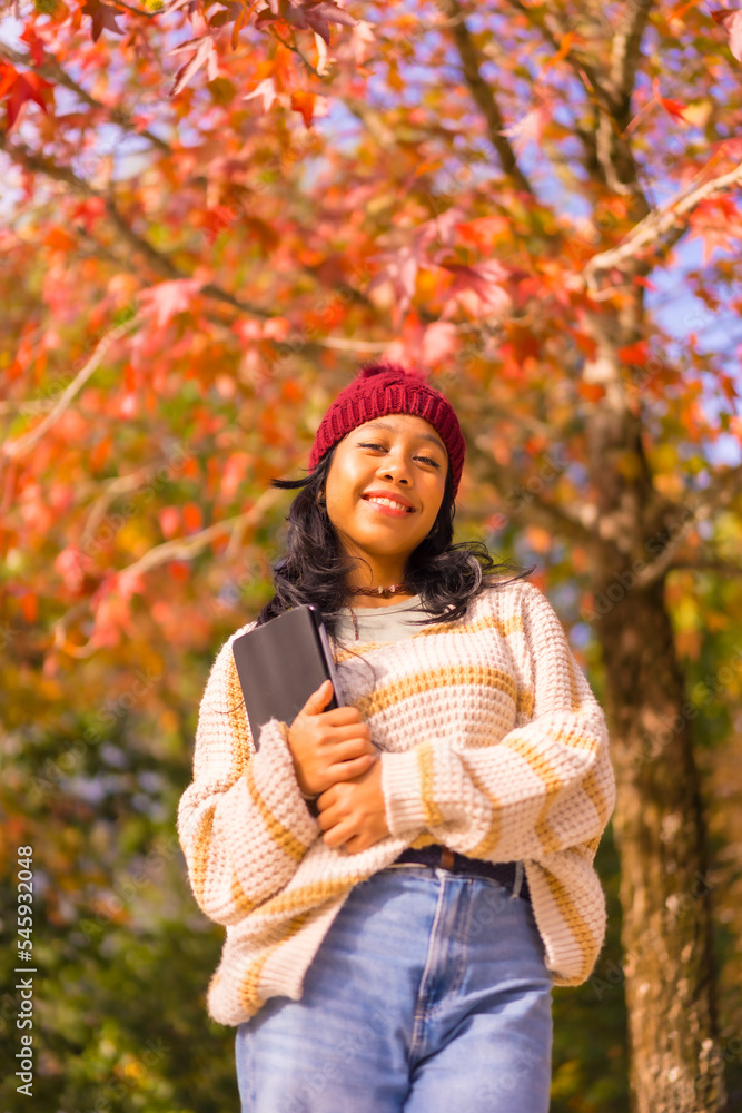 Portrait of asian girl in autumn with a tablet smiling in a forest of red leaves, technology concept Portrait of asian girl in autumn with a tablet smiling in a forest of red leaves, technology concept
