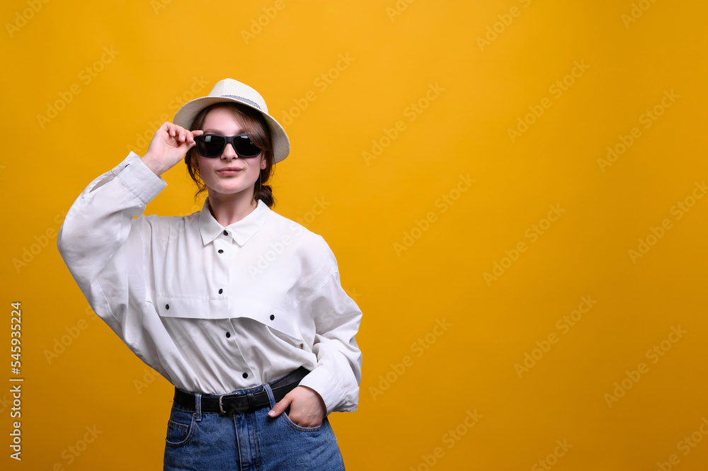 Portrait of a young woman in sunglasses and a hat on a yellow background. Summer concept, emotions, happiness Portrait of a young woman in sunglasses and a hat on a yellow background. Summer concept, emotions, happiness