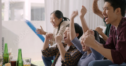 Group of young adult friend man and woman asia people sit at sofa couch joy chanting party fun game FIFA world cup live TV at home eat snack bowl drink beer bottle glass jump mad happy win exult face.