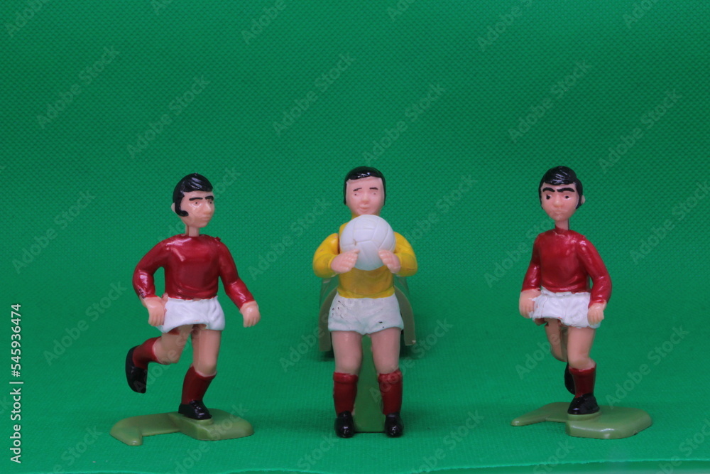 Football Soccer figures in red and white , with black football boots ,   with goalkeeper in yellow and white with red socks, on green background, vintage soccer action game figures. 