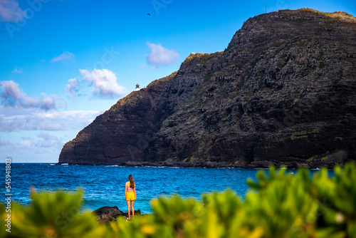 beautiful girl stands on the rocks in makapuu beach park admiring the sunset over makapu'u lighthouse on oahu, hawaiian islands; holiday in hawaii