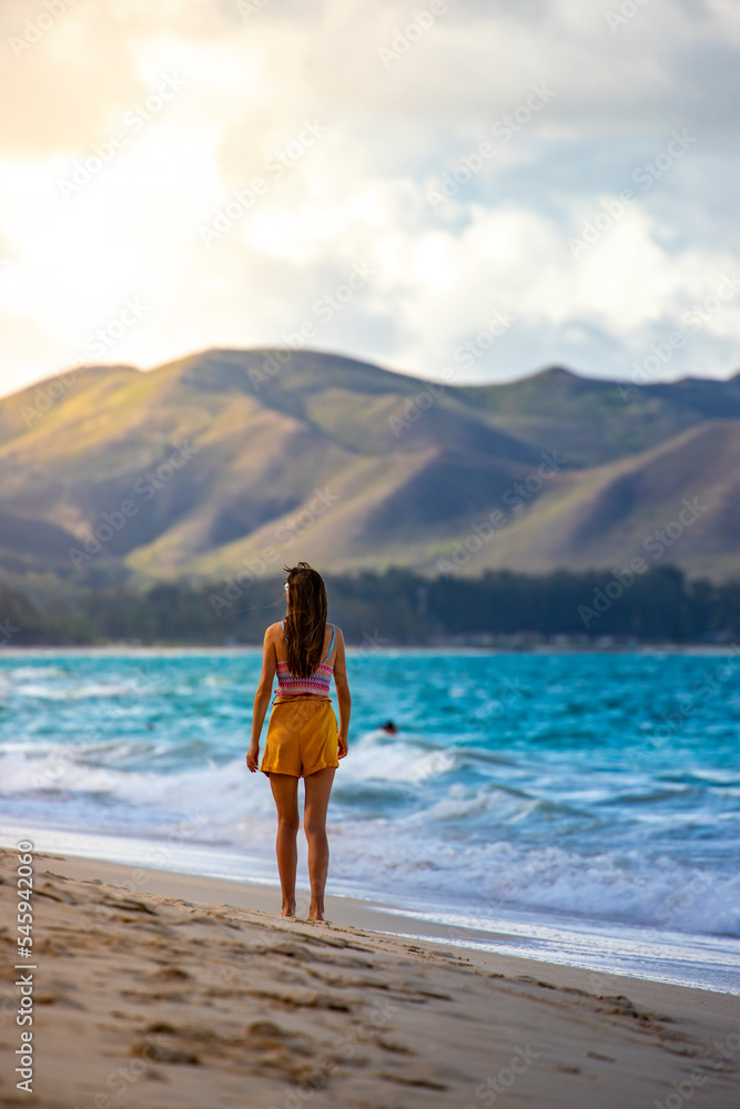 A beautiful girl walks along a paradise beach on the Hawaiian island of oahu overlooking the mighty green mountains; holiday in hawaii